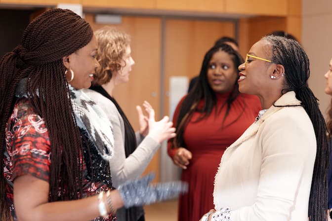 Lola Eniola-Adefeso smiles mid conversation with a colleague while and Kelly Stevens chats with friends and colleagues in the background.