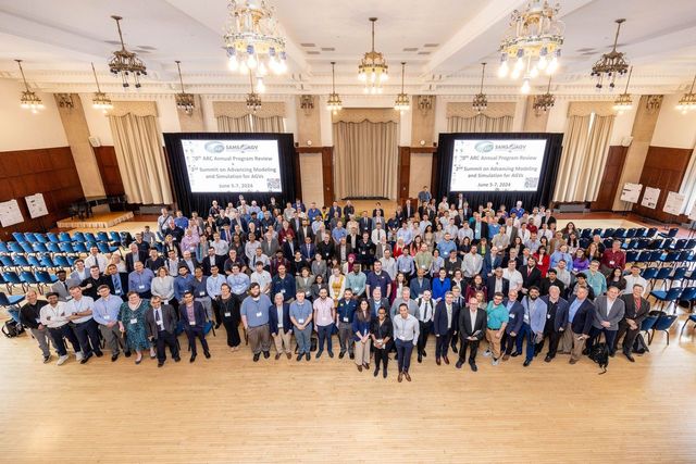 Large group of people in an auditorium with chandeliers, two large screens, and blue chairs, gathered for the the 30th anniversary of the Automotive Research Center (ARC) in June, hosted by the University of Michigan.