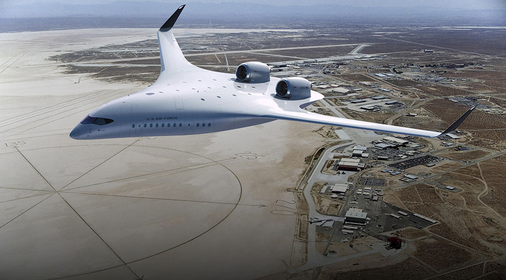 Futuristic flying wing aircraft in flight over a desert airfield. The aircraft has a broad, flat shape with no distinct body with two large jet engines on top near the rear and small upward-angled stabilizers at the wingtips.