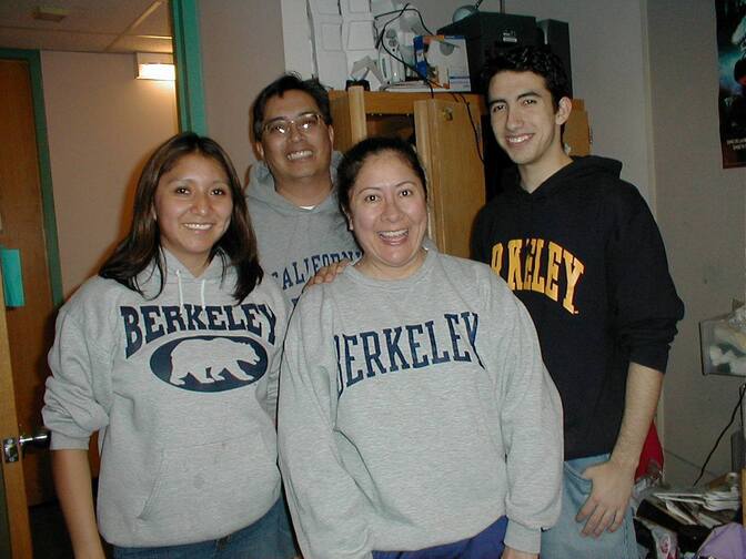 Two young women and two young men stand grinning in a dorm room, all in sweatshirts that read "Berkeley" or "California."