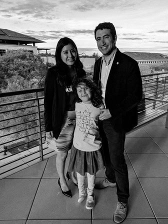  Black and white portrait of the smiling family on a balcony, the wind blowing the child's hair across her forehead.