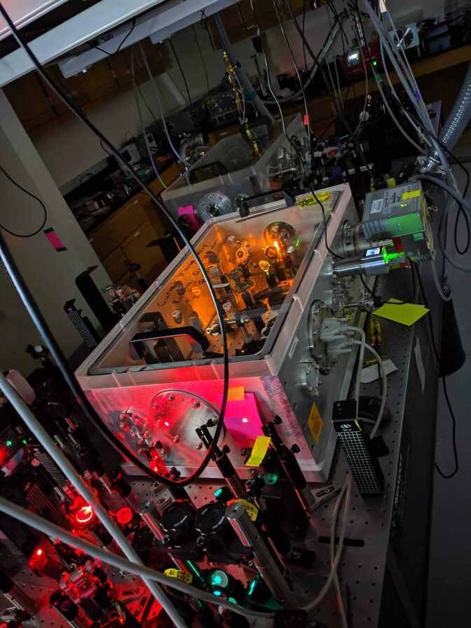  Lenses and reflectors are densely arranged in two areas on an optical table, inside a box and outside.