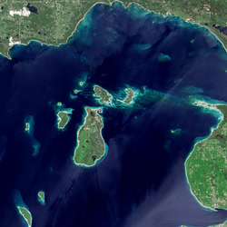  A satellite image of Beaver Island; a large green mass surrounded by the dark blue waters of Lake Michigan. Smaller islands surround Beaver Island to the north and west.