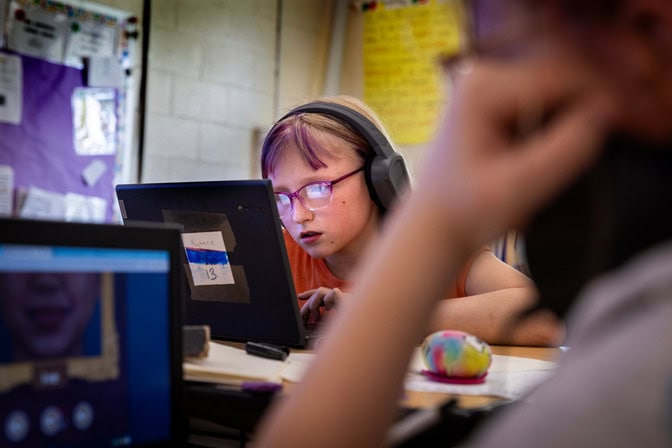 A young student leans towards her laptop screen as she strikes the keys on her keyboard.