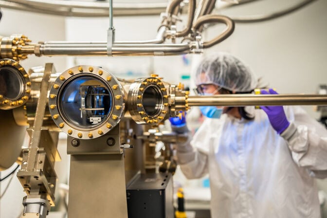 In the background, Pan shines a light into the device. In the foreground are multiple portholes and tubes in silvery metal.