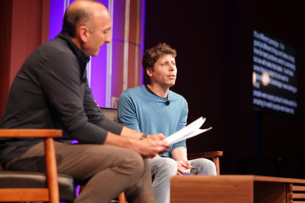 Dan Feder looks over questions on a piece of paper, while Sam Altman talks to the crowd