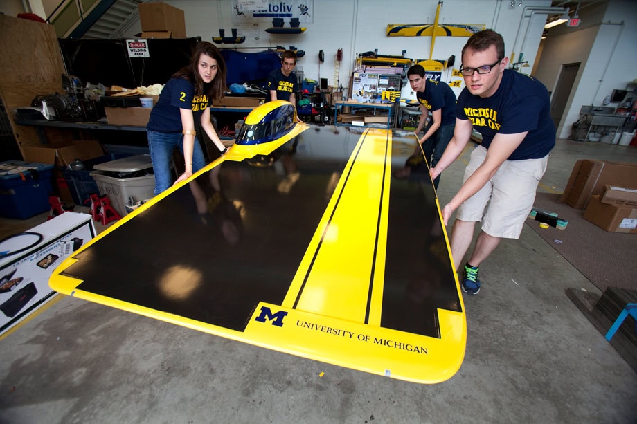 Four students carefully lift a solar car