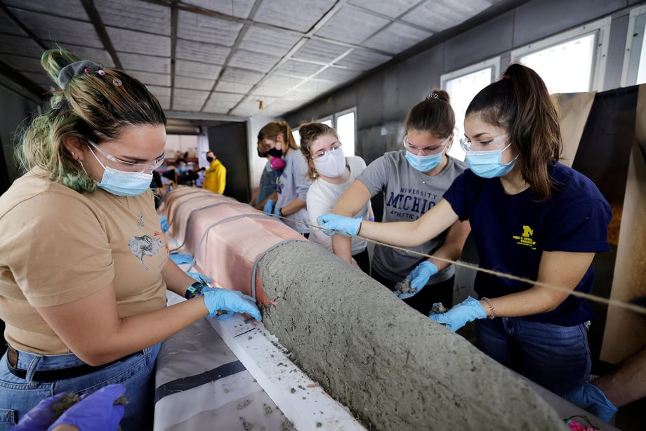 Students, wearing proper lab gear, create their concrete canoe.