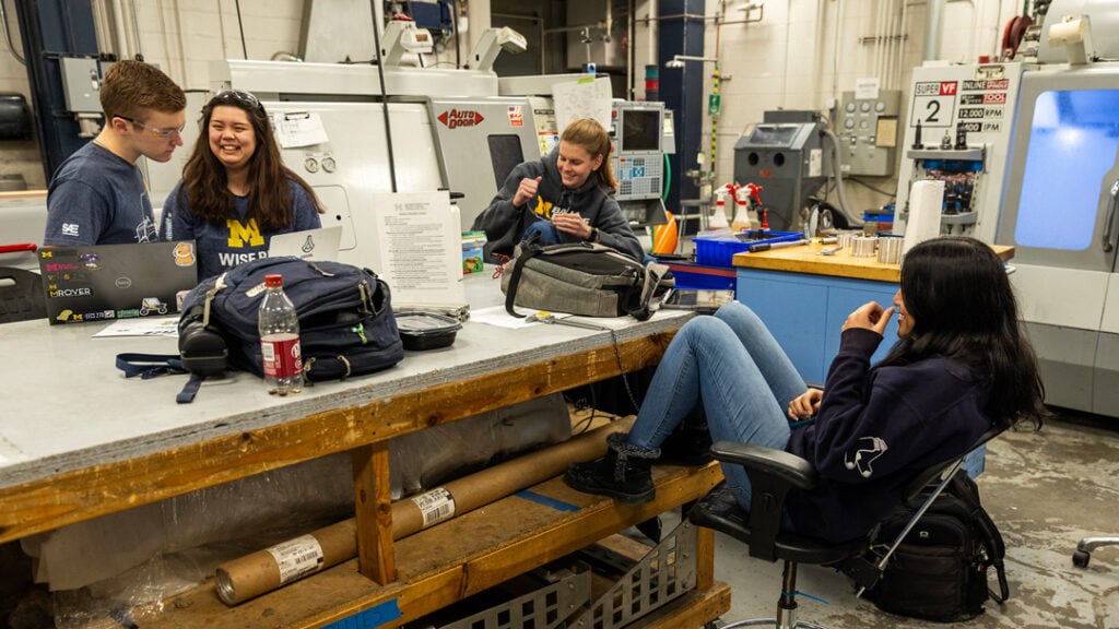 Four students sit at a large table socializing