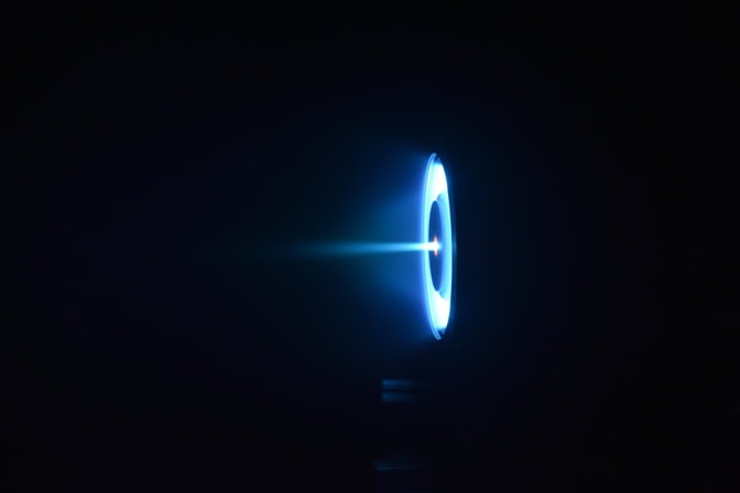 The thruster glows as a pale blue ring with a disk-shaped shadow in middle, and a blue ray streaking out from the center.