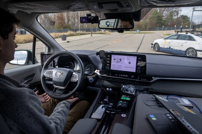 Interior of a car with autonomous driving features, showing the driver’s hands off the wheel and a central touch screen.