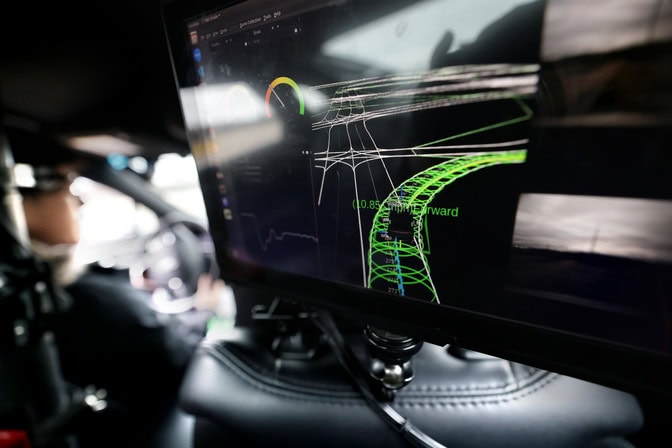 A car interior with a screen showing a 3D wireframe model of a roadway.