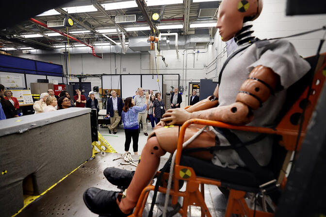 Crash test dummy in a testing facility with a group of people observing.