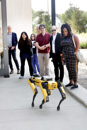 A group of people observing a yellow robot with four legs outdoors.