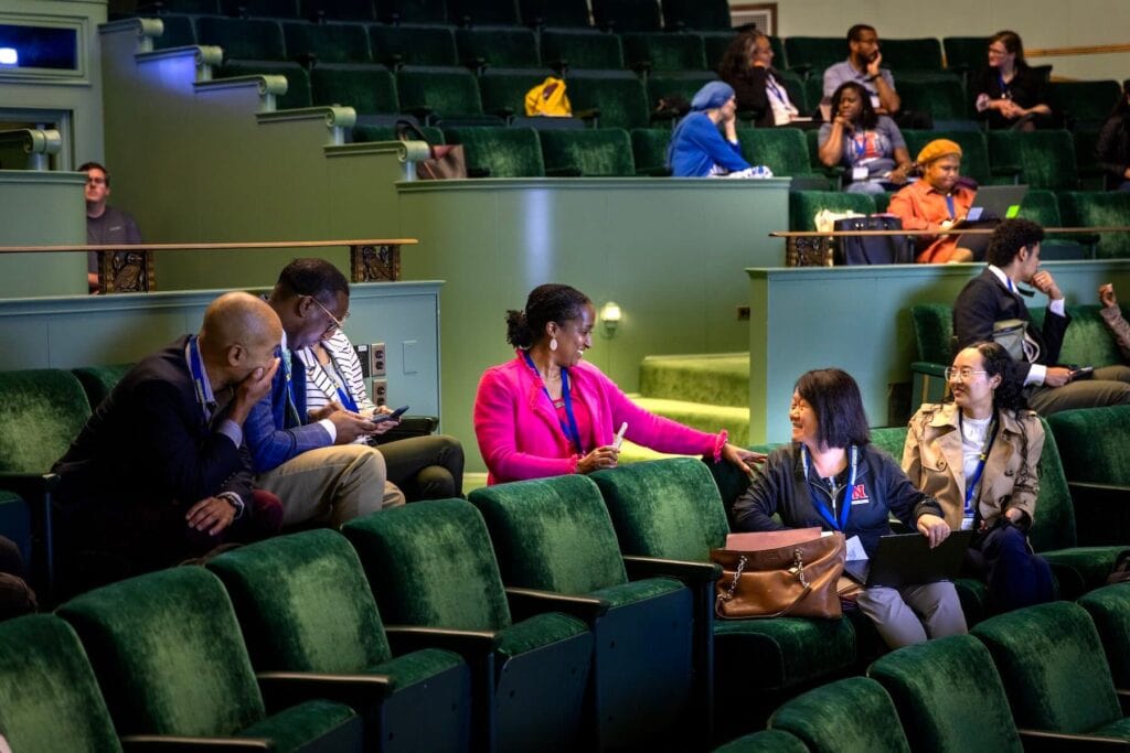 Six professionals turning around in their seats in velvet-green seats of an auditorium to chat and listen. 