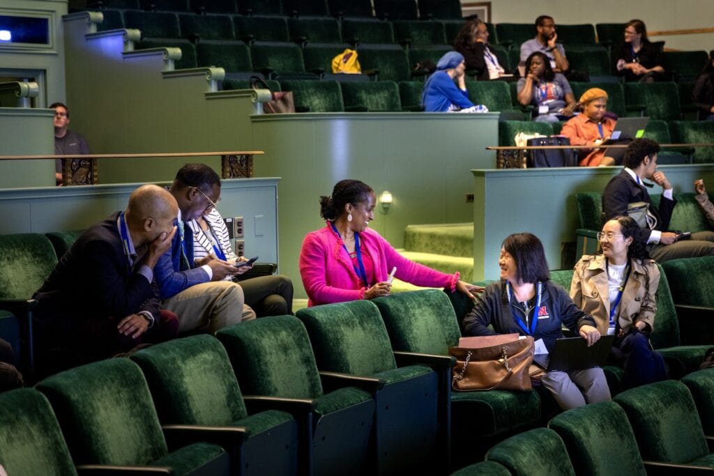 Six professionals turning around in their seats in velvet-green seats of an auditorium to chat and listen. 