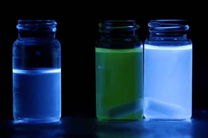 Three vials with luminescent liquids in blue, green, and blue, glowing under UV light.