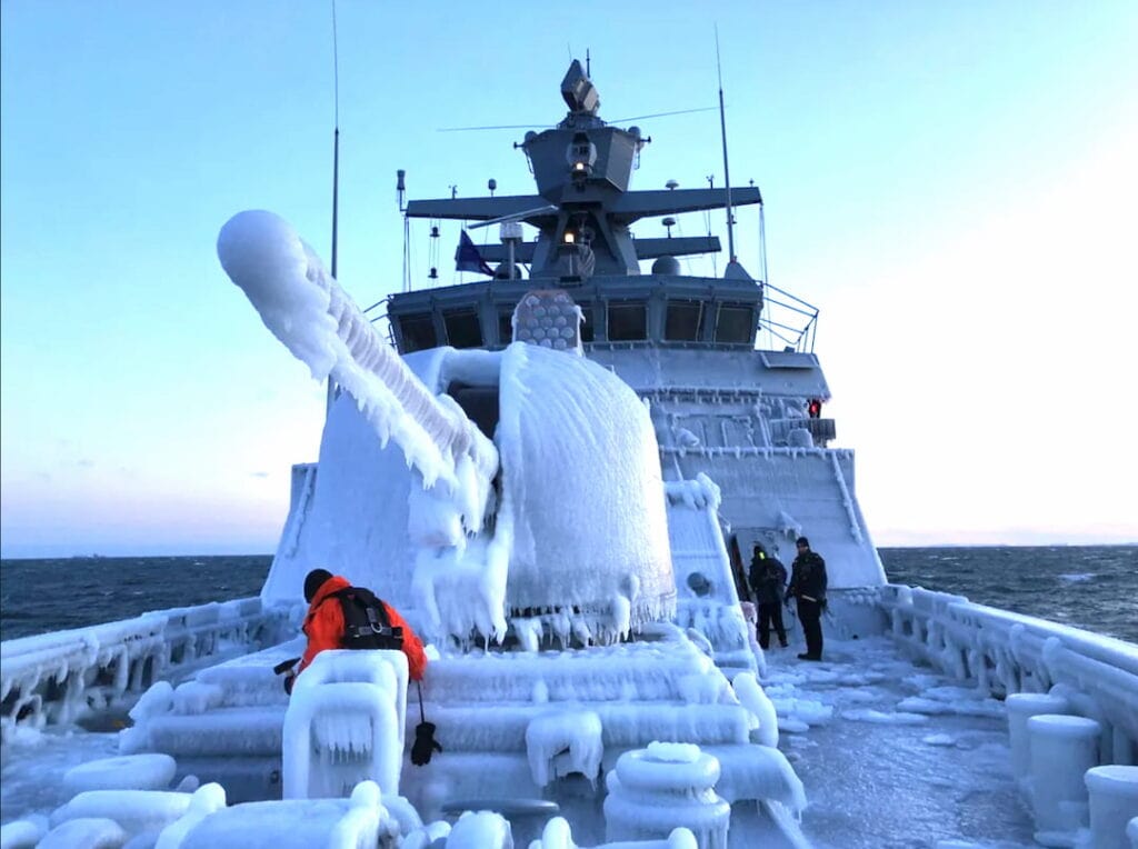 A military battle ship with a large cannon. The deck and cannon are covered in ice and the barrel of the cannon has icicles forming