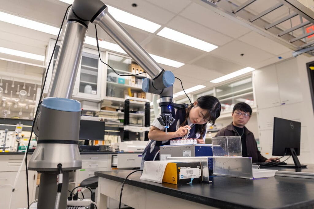 Two graduate students working in a lab with a silver robotic arm