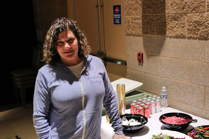  A woman stands near a table bedecked with dishes of salad, a bowl of pickled onions, and a garlic dip. Cans of soda are neatly arranged at the end of the table.