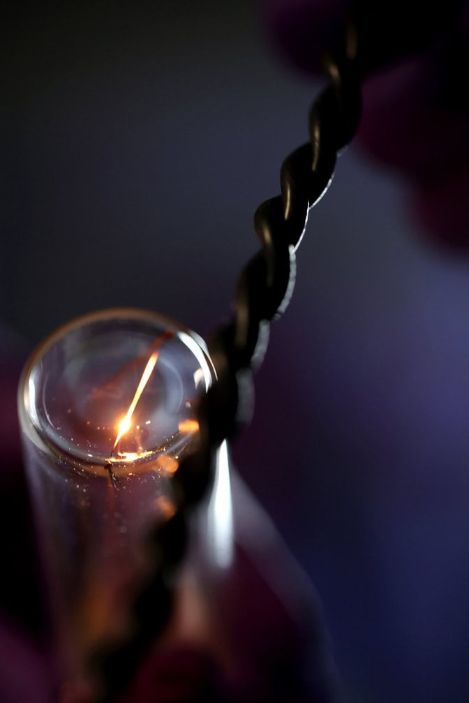 A wire glows bright gold inside a glass tube. Beside it, two black wires are twisted together.