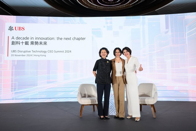 Zhen Xu stands with two women on a stage with a screen that displays "a decade in innovation: the next chapter" for the UBS Disruptive Technology CEO Summit 2024, hosted in Hong Kong.