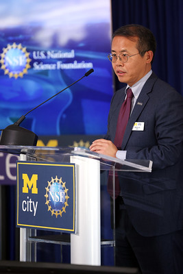 Henry Liu speaking at a podium in front of a University of Michigan Mcity backdrop.