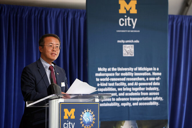 Henry Liu speaking at a podium in front of a University of Michigan Mcity backdrop.