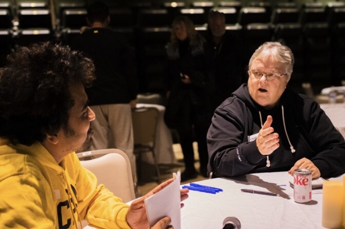 A man holding a stack of survey forms sits at a table with a woman.