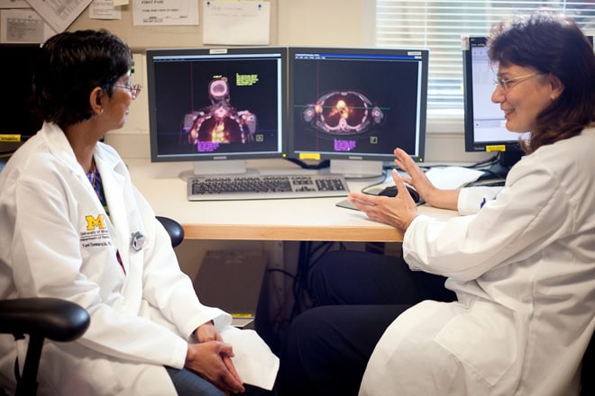 Two medical staff in lab coats review scans on a monitor