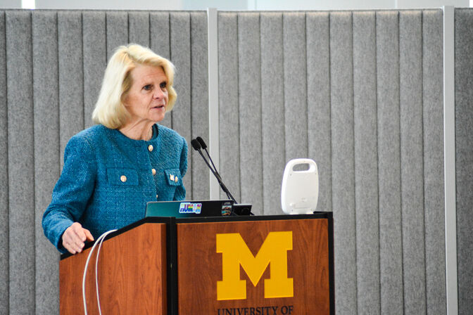 Karen Thole speaking at a podium with the University of Michigan block "M" logo on the front.