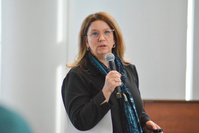 Suzanne Coffey speaking to an audience while holding a microphone.