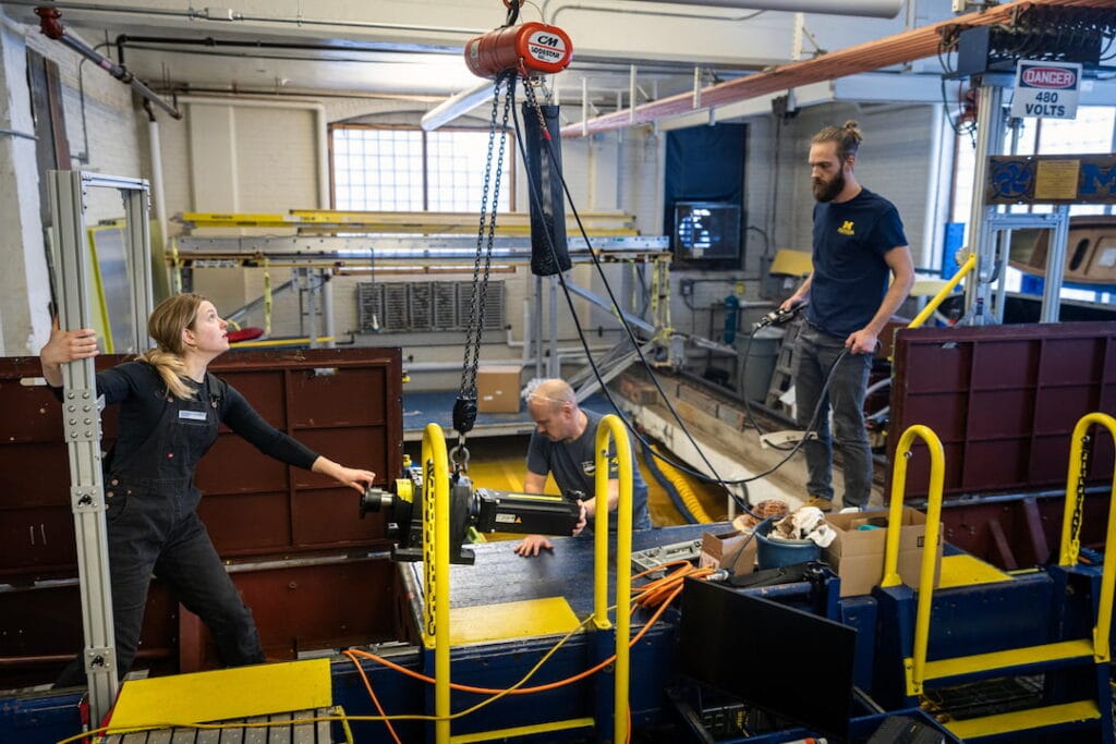 3 people lowering a motor onto a platform inside a lab.