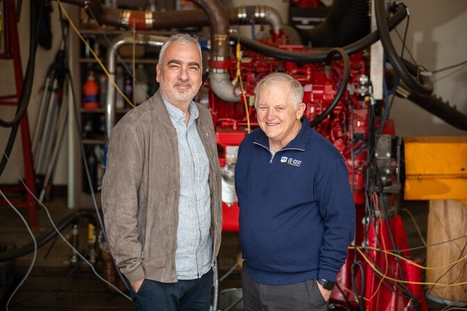 Georgios Karavalakis and Wayne Miller pose in front of mechanical engineering equipment in a lab setting. 