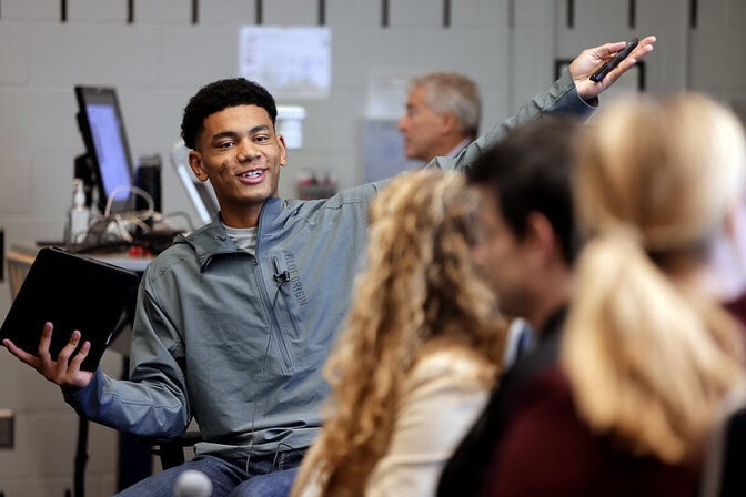 Elijah Simpson smiles as he speaks to three other students, with an arm outstretched in gesture.