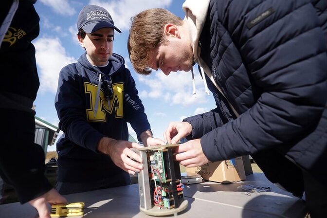 Nurick holds a cylindrical insert with green electronics boards and red wires while Nielsen makes final adjustments.