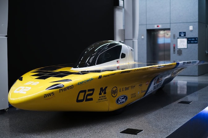 Millennium is parked in the atrium of a building with a gray, linoleum floor. Its sleek yellow body gleams as it reflects the atrium's fluorescent lights.