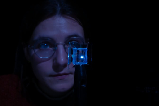 Claire Arneson holds the transparent square with the glowing blue rectangle, her face illuminated by its light