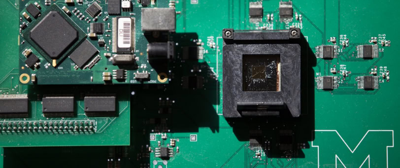 A green circuit board with multiple microchips and a cracked square component.