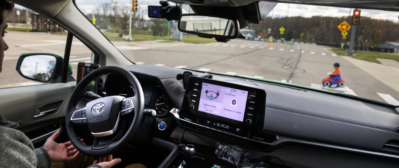 Inside a connected vehicle, a driver pauses at a cross walk as a prop pedestrian crosses in front of the vehicle