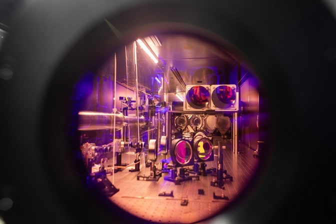 The circular glass optics and silvery metal mounts that create the laser path appear tinted pink through the round window of the crystal.