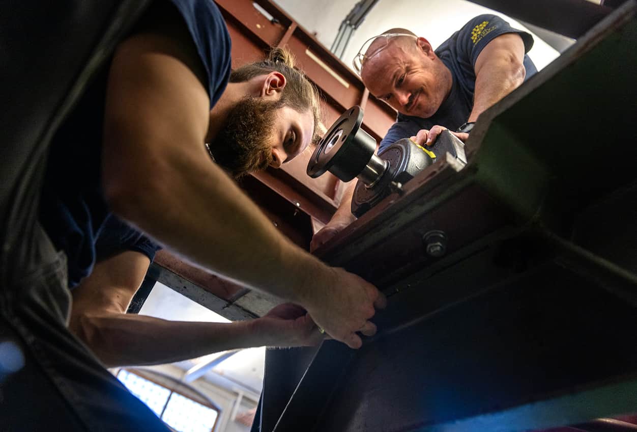 Two individuals work together to install a new motor onto a large mechanical carriage in a research facility.