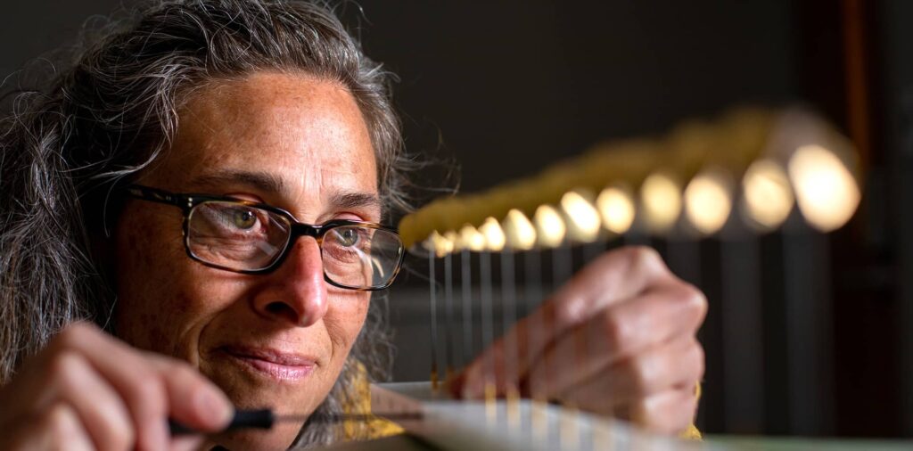 A woman in glasses closely examines a row of small objects inside a laboratory.