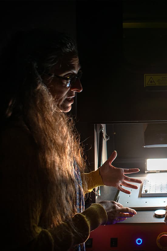 Side portrait of Sallee Klein in a dark lab with a light source coming from the equipment infront.