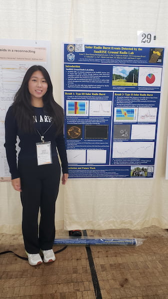 A teenage girl stands smiling in front of an academic poster featuring solar radio burst data.]