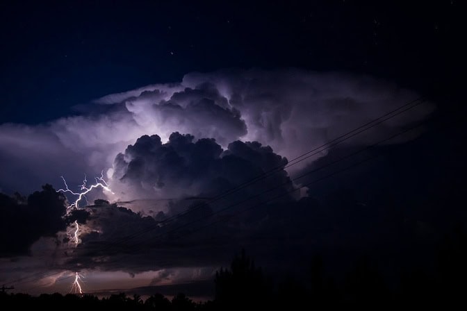 Dramatic storm clouds at night, lit up by lightning forks.