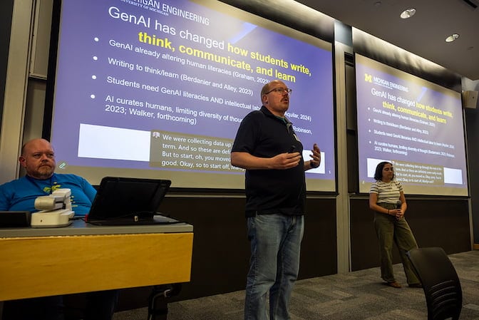 A wide shot of a man and woman standing in front of large screens with slides on them. The slides say "Gen AI has changed how students write, think, communicate and learn."