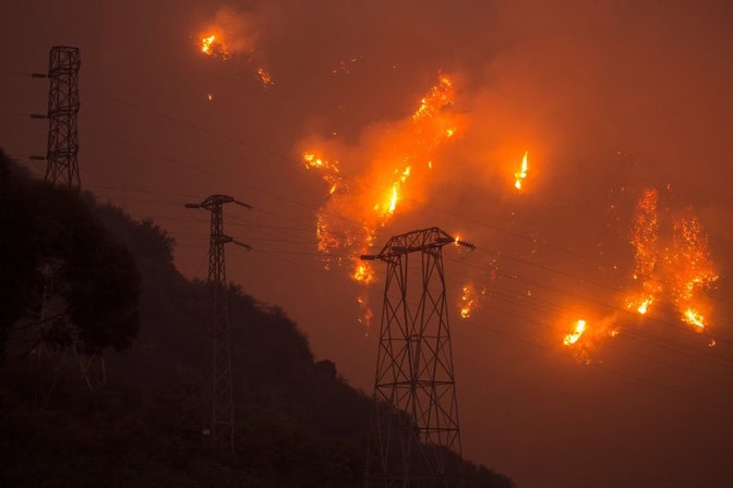 Pylons silhouetted on a hillside, the background smoky gray with bright spots of orange fire