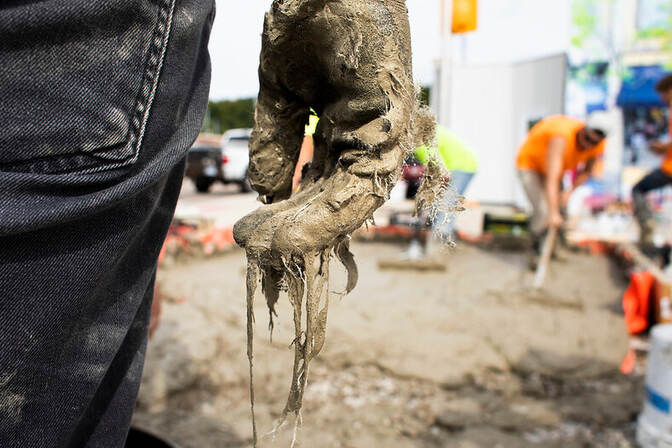 Close-up of a mud-covered hand with people working in the background.