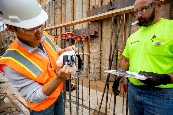 Two construction workers at a building site examining a device on a building site.